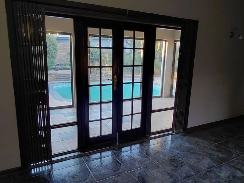 Spacious living area featuring dark tiled flooring and classic French doors providing direct access to the outdoor pool area.