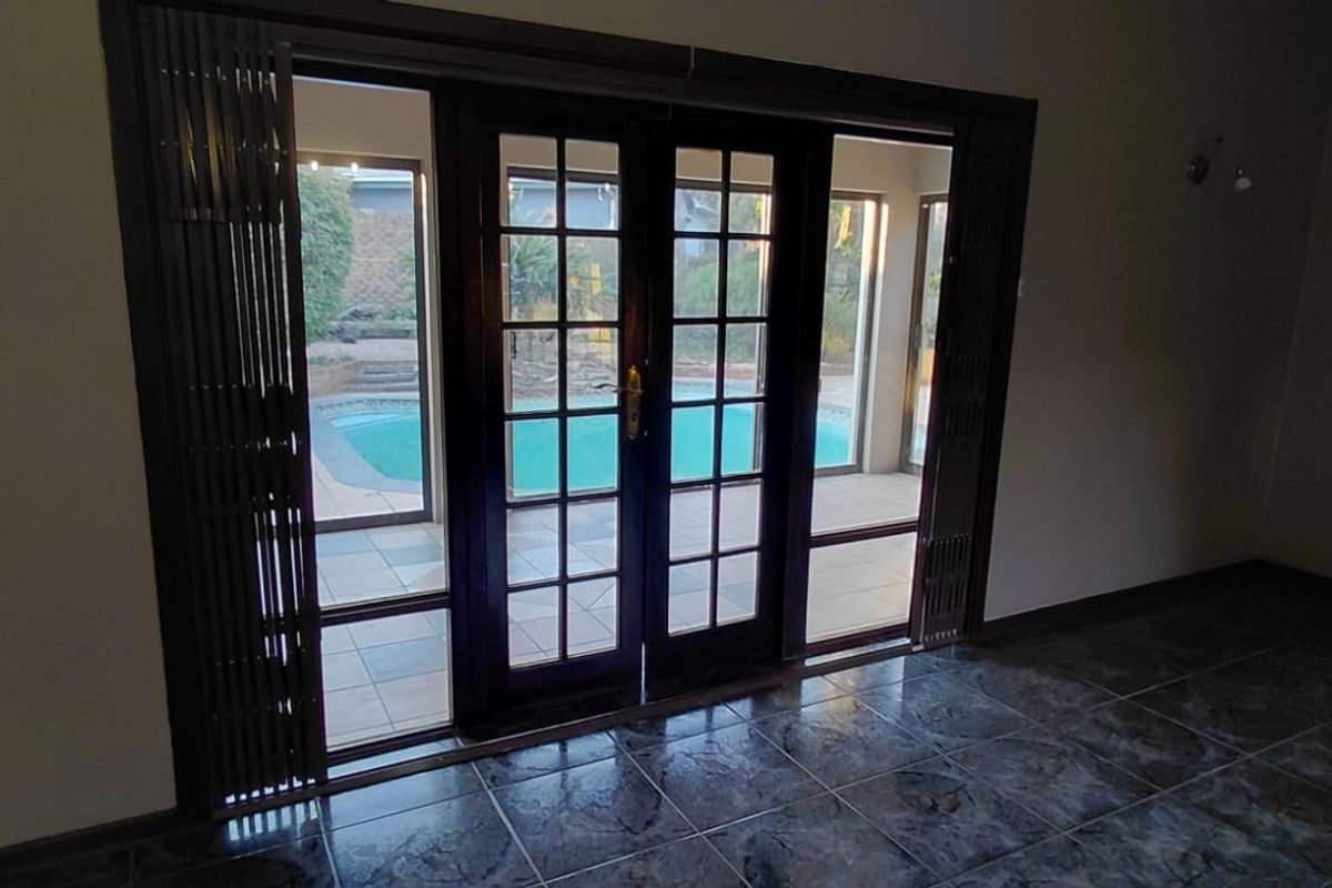 Spacious living area featuring dark tiled flooring and classic French doors providing direct access to the outdoor pool area.