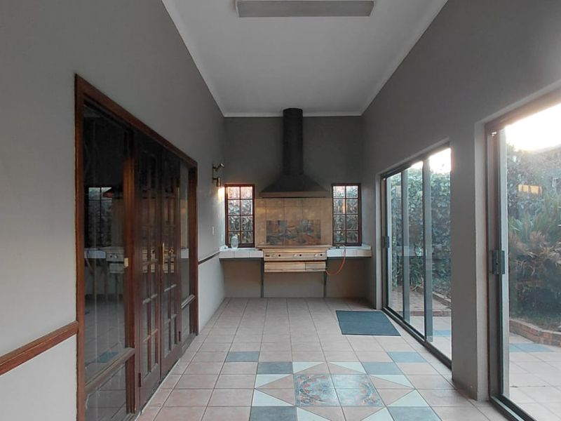 Covered patio area featuring a built-in braai with extractor hood, tiled flooring, and large sliding glass doors providing access to the garden.