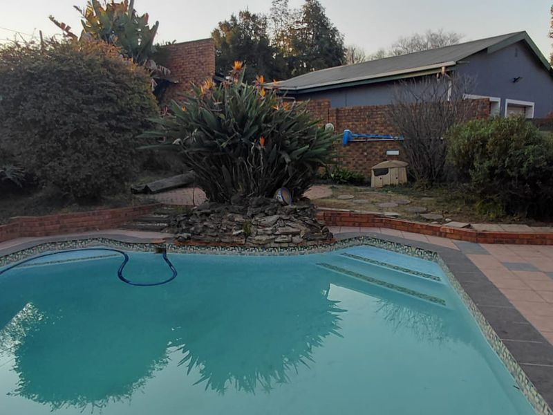 Outdoor pool area featuring a swimming pool, brick paving, and a stone feature planter set within a private garden space.