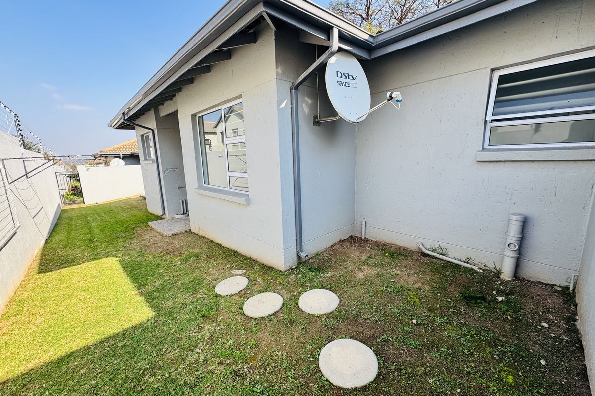 A view of the rear exterior of the townhouse, featuring a small lawn area, satellite dish, and paved stepping stones.