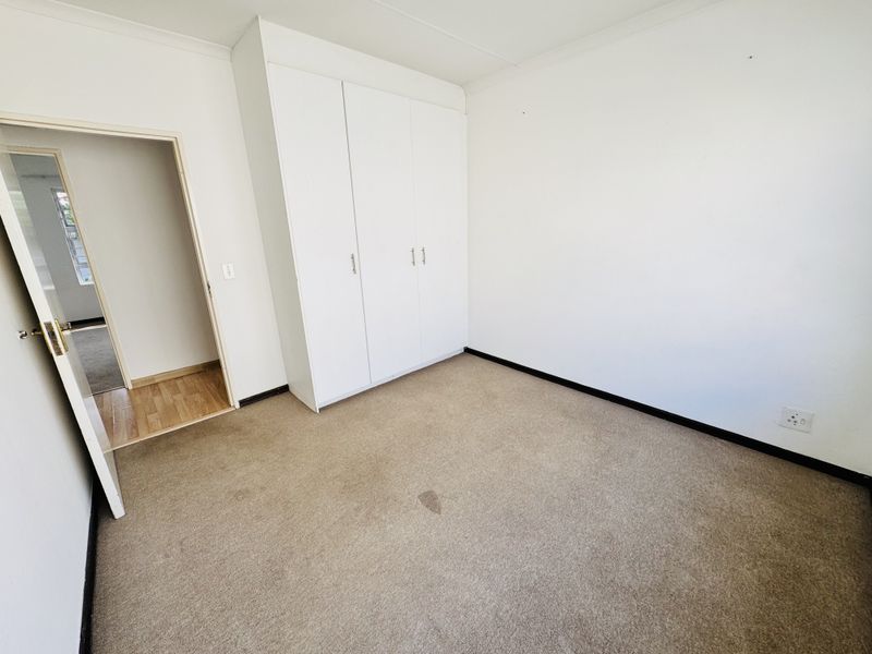 A vacant bedroom featuring built-in cupboards, neutral walls, and carpeted flooring, with an adjacent hallway entrance.