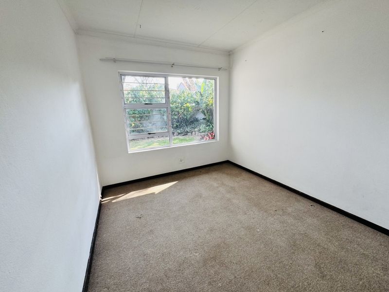 A vacant bedroom featuring neutral walls, carpeted flooring, and a large window overlooking the garden.