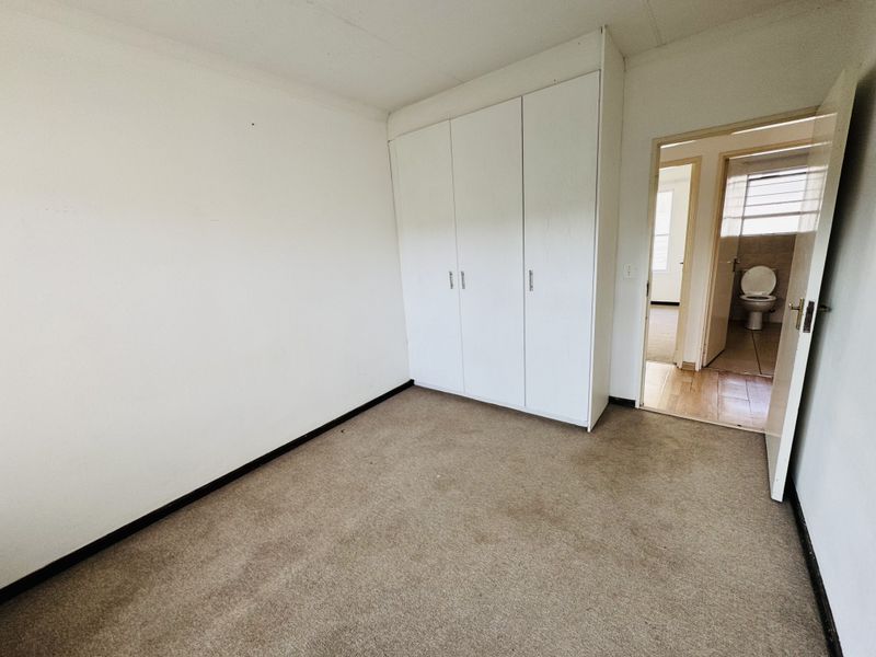 A vacant bedroom featuring built-in cupboards and carpeted flooring, with an adjacent view into a bathroom area.