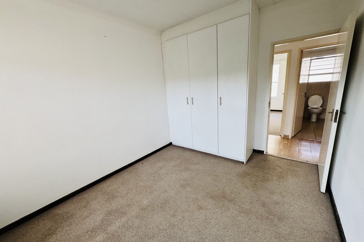 A vacant bedroom featuring built-in cupboards and carpeted flooring, with an adjacent view into a bathroom area.