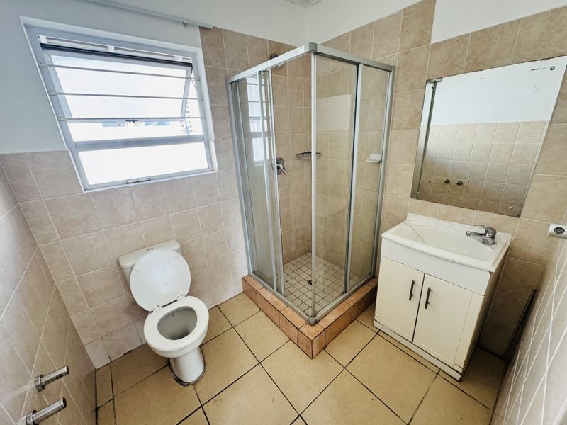 A functional bathroom featuring a corner shower enclosure, a vanity with integrated basin, a toilet, and tiled walls and flooring.