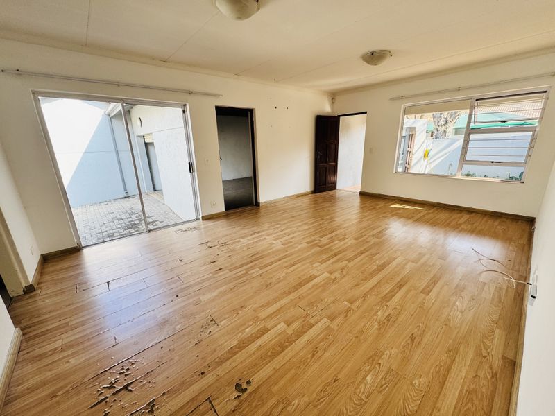 Spacious living area featuring light wood-look laminate flooring, large sliding glass doors leading to a patio, and natural light through multiple windows.