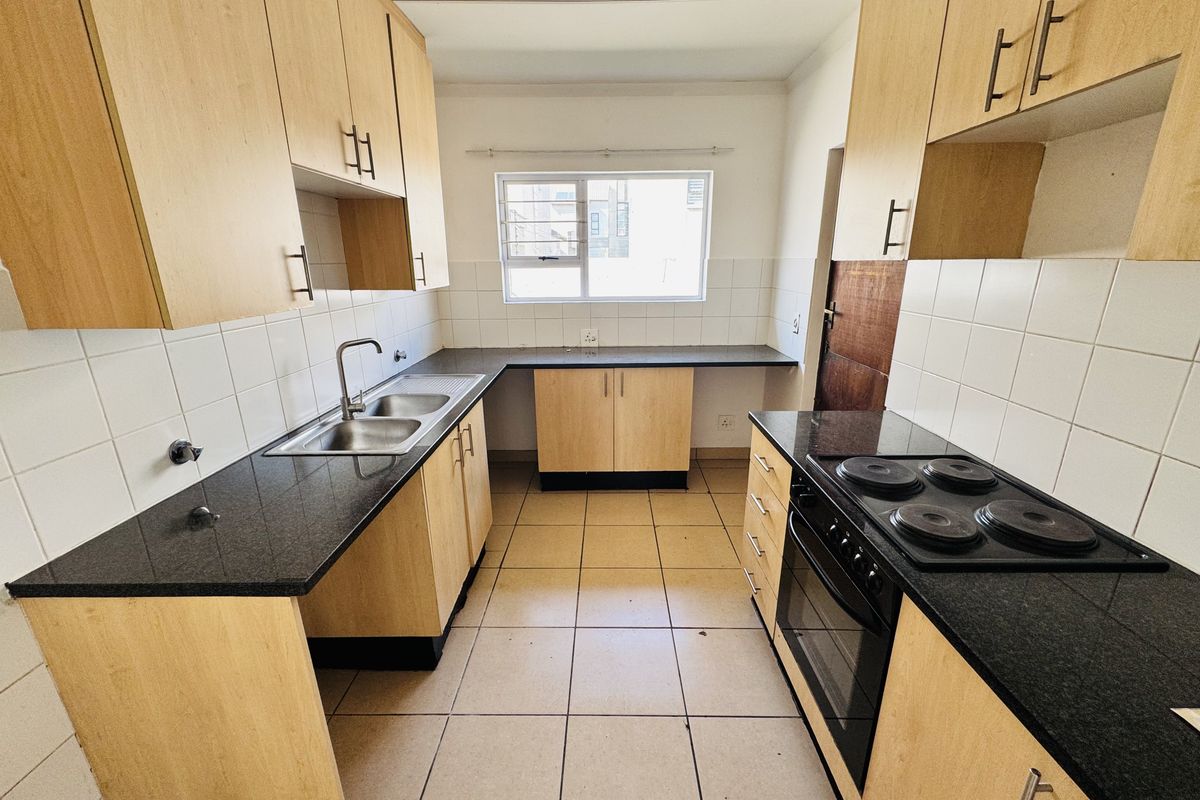 A functional kitchen featuring light wood cabinetry, dark granite countertops, a built-in electric stove and oven, and tiled flooring.