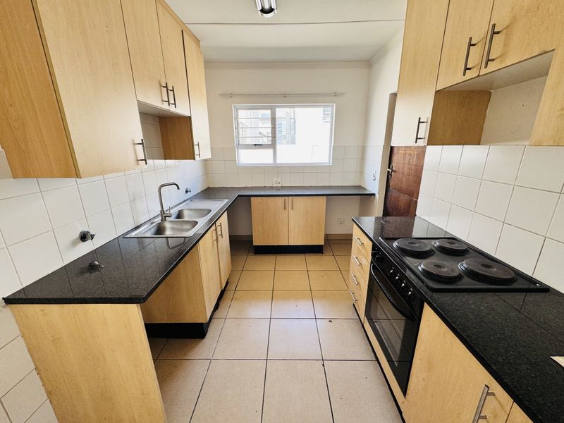 A functional kitchen featuring light wood cabinetry, dark granite countertops, a built-in electric stove and oven, and tiled flooring.