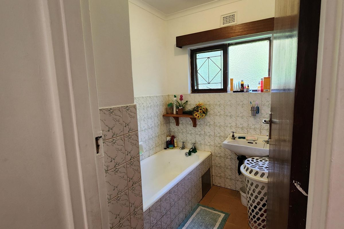 A functional bathroom featuring a built-in bathtub, wall-mounted basin, and tiled flooring, offering a classic layout with potential for modern updates.
