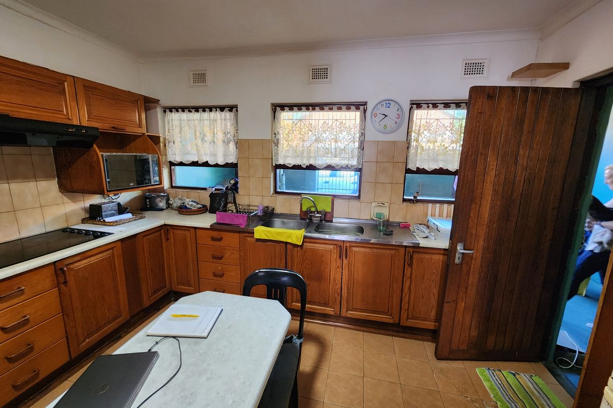 A functional kitchen featuring traditional timber cabinetry, tiled splashbacks, integrated cooktop, and double stainless steel sink with ample counter space.