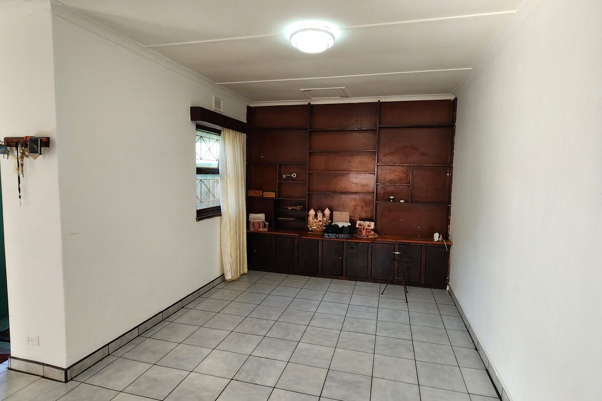 A bright living area featuring neutral floor tiles and extensive built-in wooden shelving, offering versatile storage and display space.