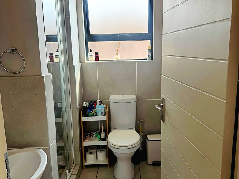 A functional bathroom featuring a shower enclosure, pedestal basin, and toilet with neutral wall and floor tiling.