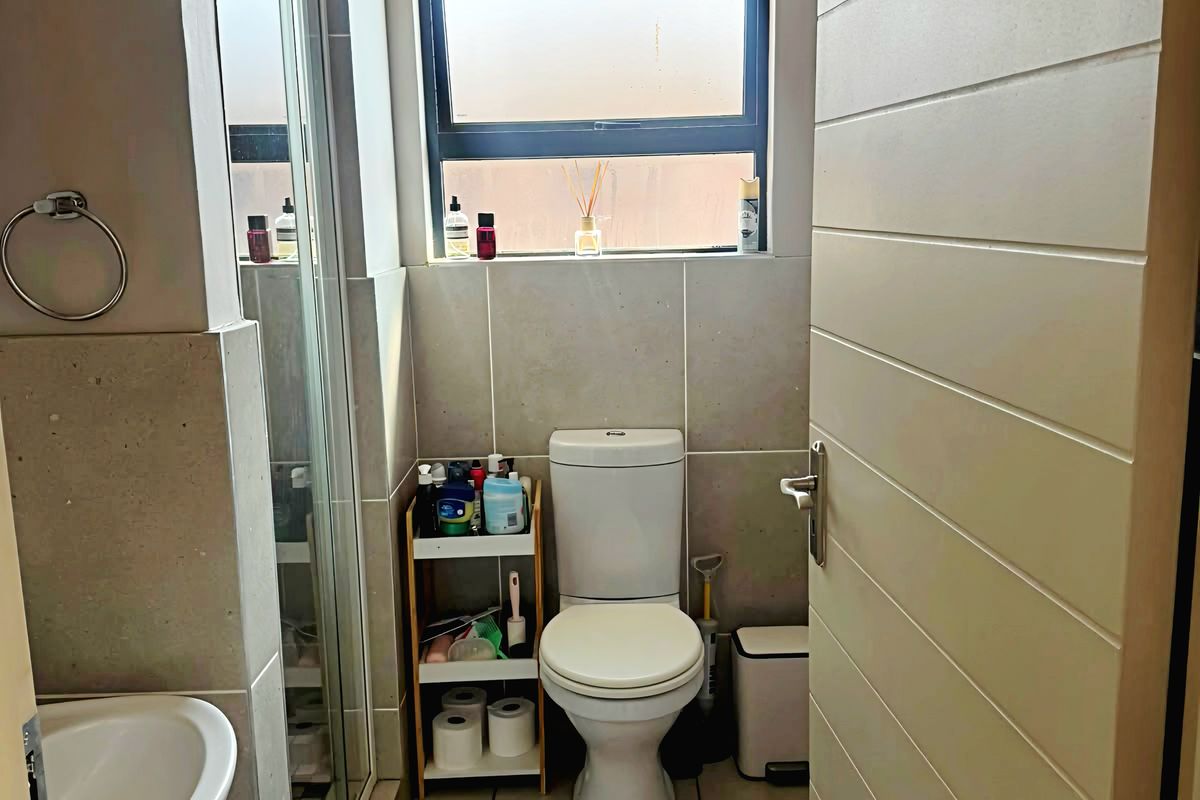 A functional bathroom featuring a shower enclosure, pedestal basin, and toilet with neutral wall and floor tiling.