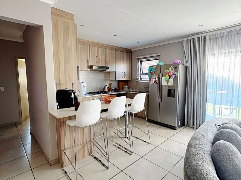 Modern open-plan kitchen featuring light wood cabinetry, stone countertops, a breakfast bar, and tiled flooring, seamlessly integrated with the living area.