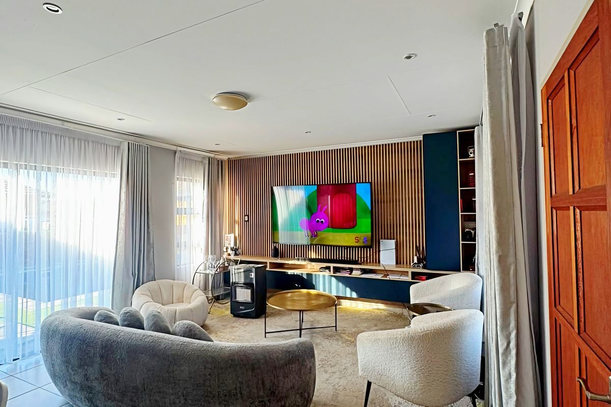 A modern living room featuring a stylish slatted timber accent wall, built-in media cabinetry, tiled flooring, and large sliding doors providing ample natural light.