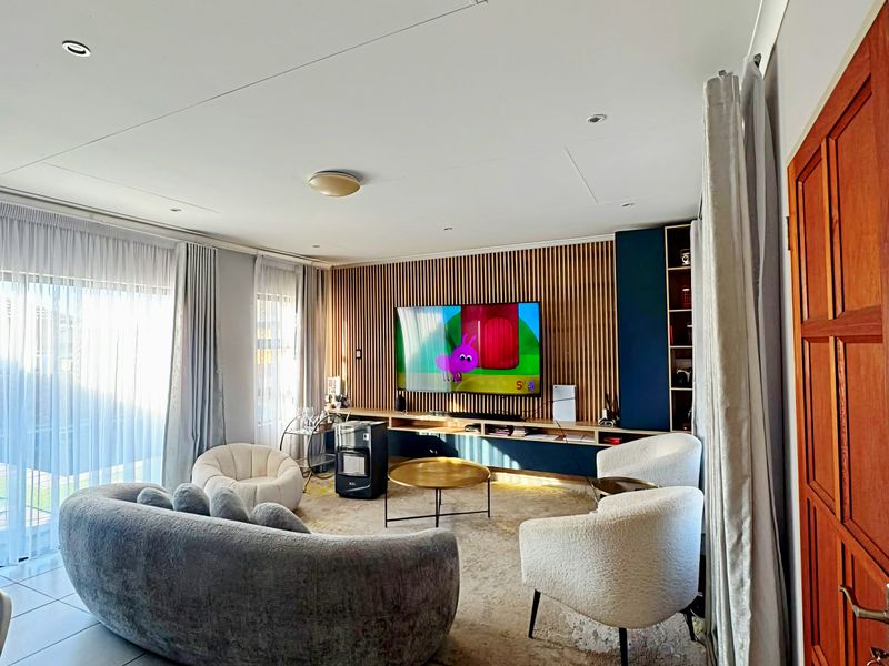 A modern living room featuring a stylish slatted timber accent wall, built-in media cabinetry, tiled flooring, and large sliding doors providing ample natural light.