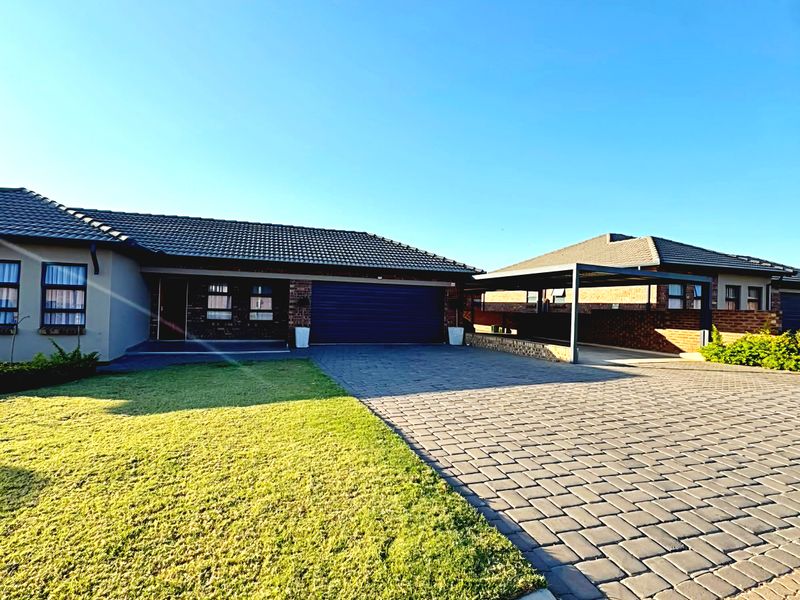 Front view of a modern house featuring a paved driveway, double garage, and a covered carport, set against a well-maintained lawn.