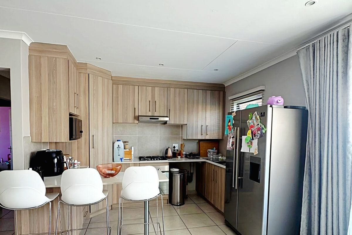A functional kitchen featuring light wood-finish cabinetry, tiled flooring, a breakfast bar, and integrated appliances, offering a clean and practical cooking space.