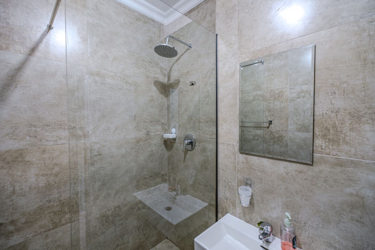 Modern bathroom featuring floor-to-ceiling stone-look tiling, a glass-enclosed walk-in shower with rainfall showerhead, and a wall-mounted vanity mirror.