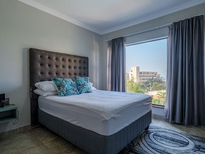 A well-maintained bedroom featuring tiled flooring, large windows with curtains, and a view of the surrounding area.