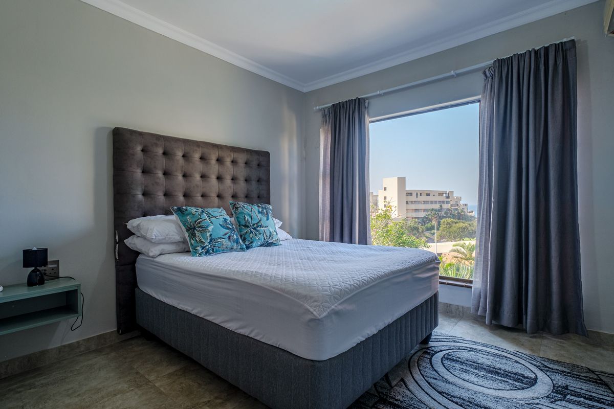 A well-maintained bedroom featuring tiled flooring, large windows with curtains, and a view of the surrounding area.