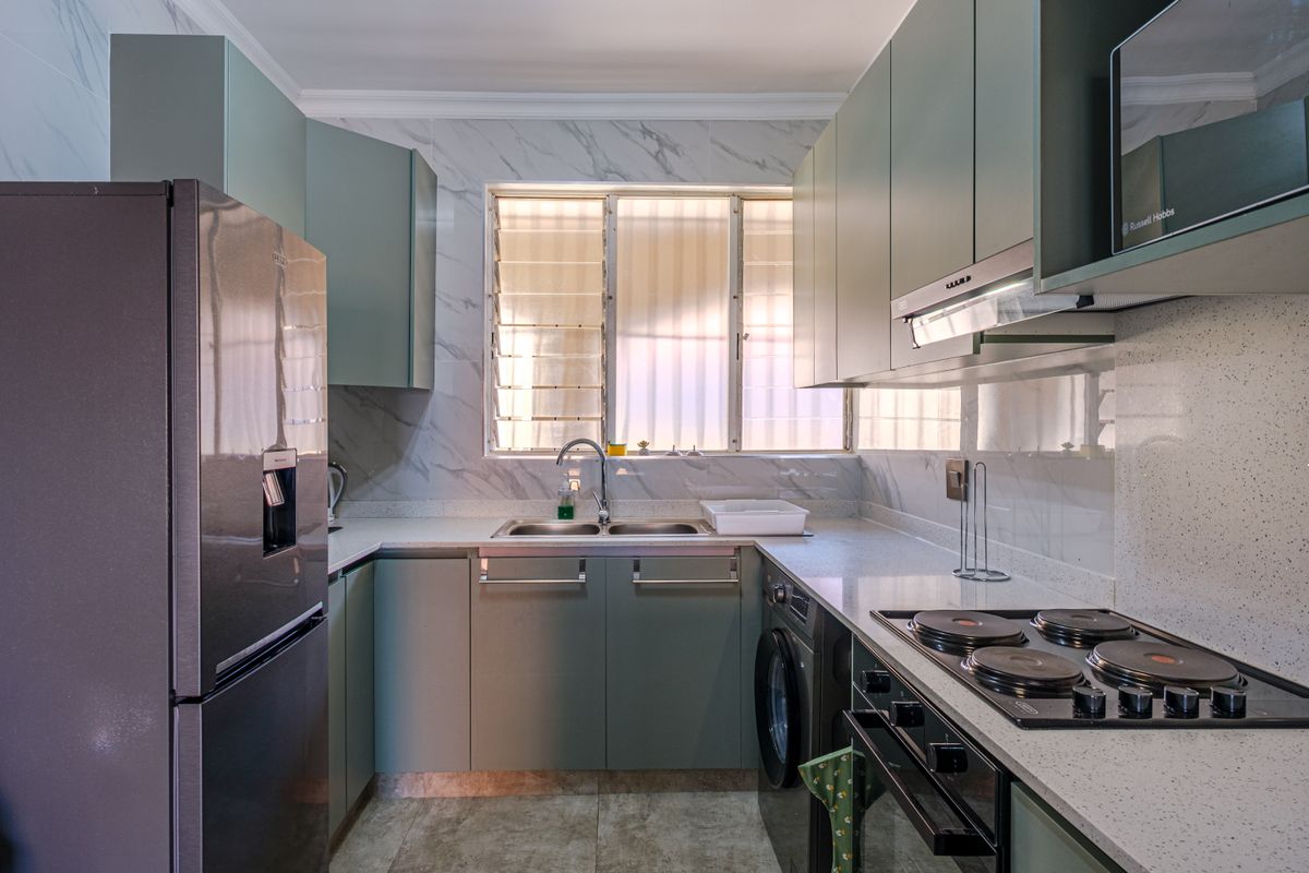 Modern kitchen featuring sage green cabinetry, stone-look countertops, marble-effect wall tiles, a built-in oven, hob, extractor fan, and integrated laundry plumbing.
