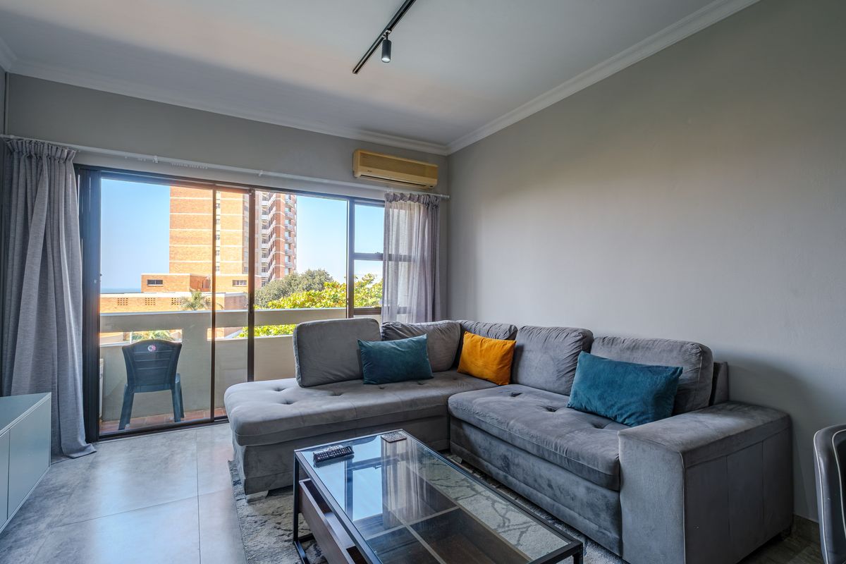 A bright living room featuring large sliding glass doors that open onto a balcony, providing natural light and an urban view.