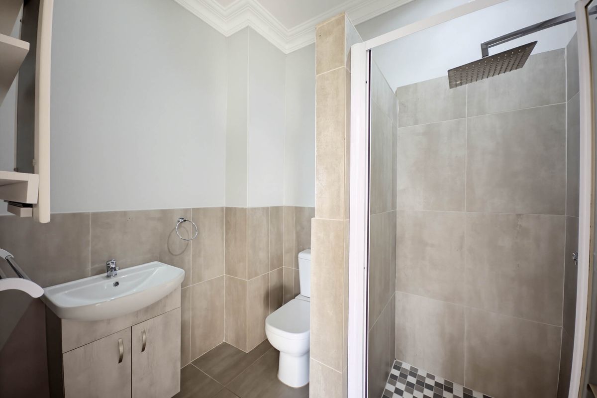 Modern bathroom featuring a walk-in shower with a rainfall showerhead, a vanity basin with storage, and a toilet, finished with neutral wall and floor tiles.