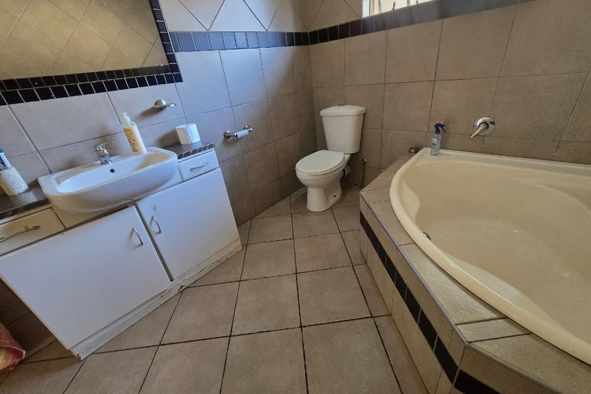 A functional bathroom featuring a built-in vanity with basin, a standard toilet, and a tiled bathtub surround with neutral wall and floor tiling.