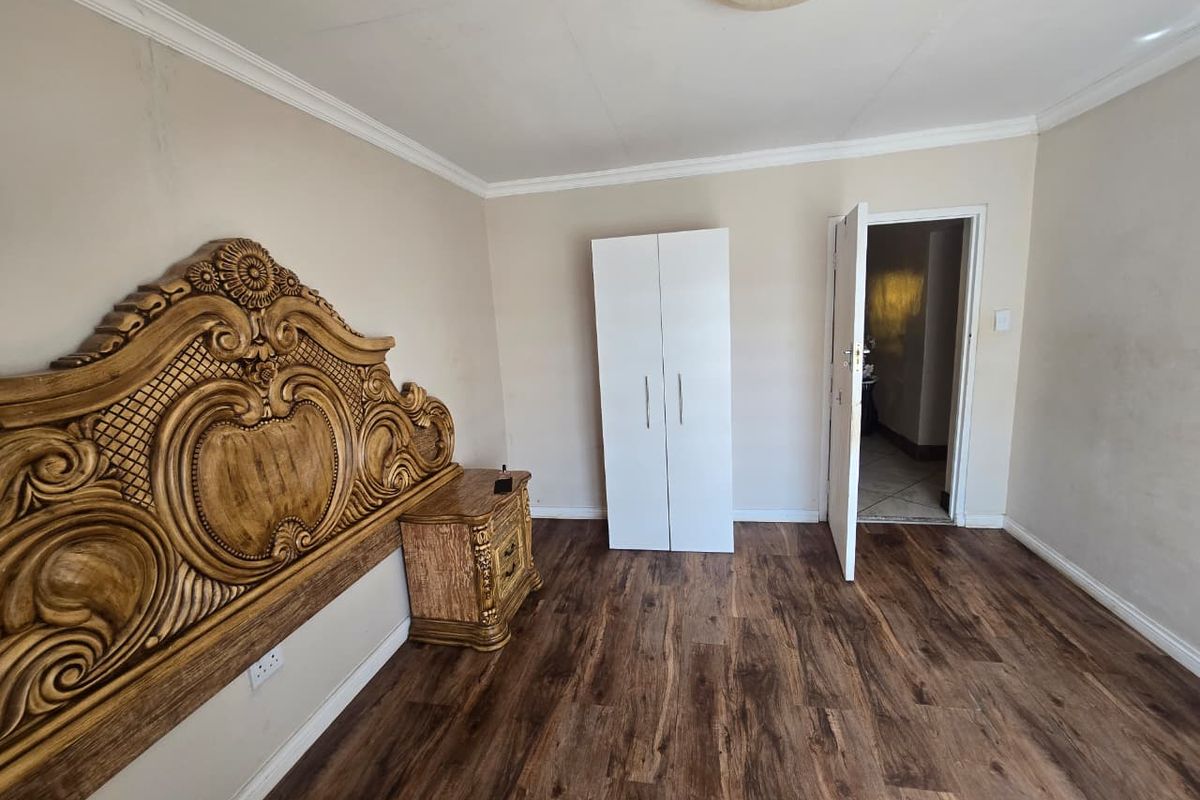 A bedroom featuring wood-look laminate flooring, crown molding, and a doorway leading to an adjacent room.