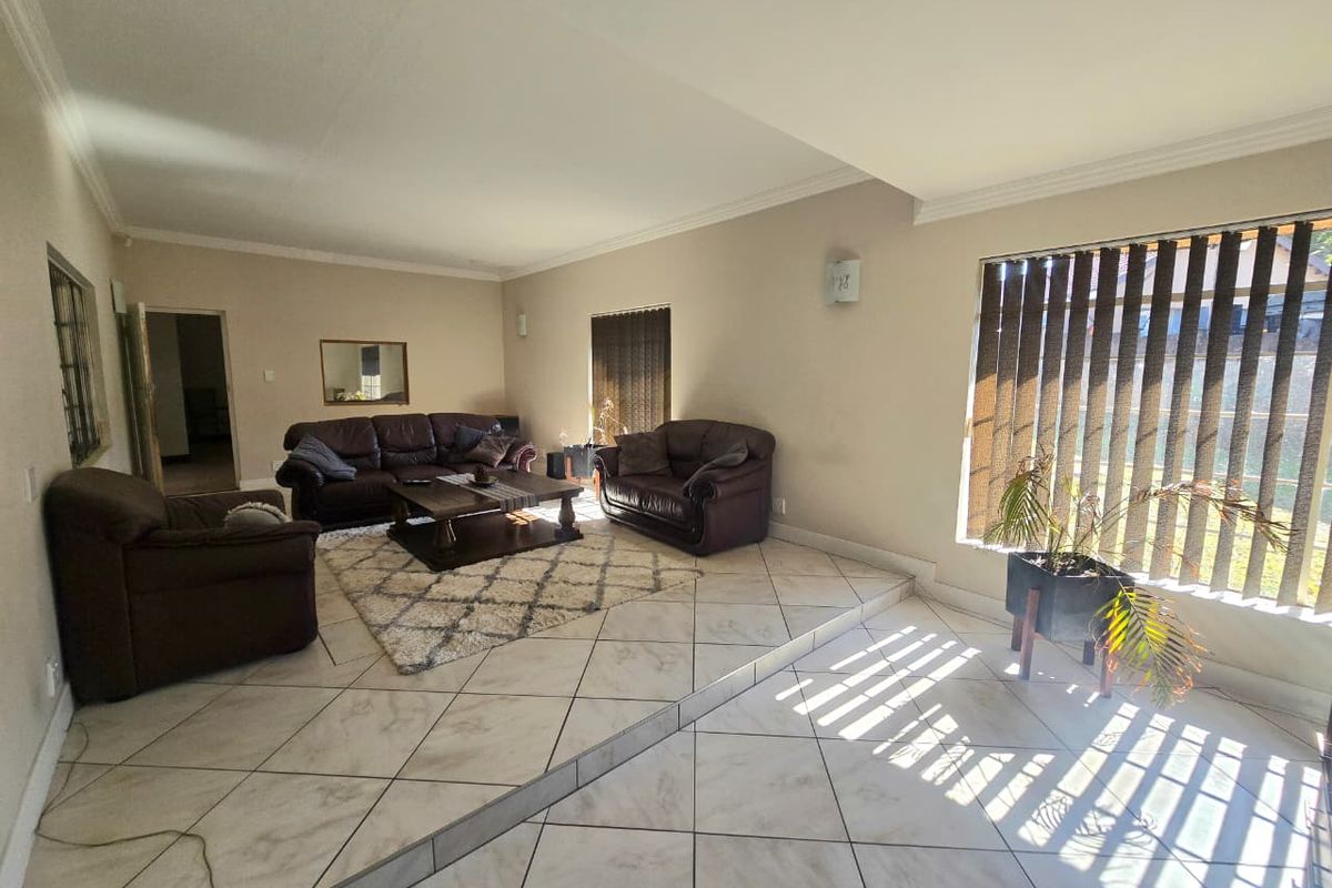 Spacious living room featuring a raised floor section, tiled flooring, and large windows with vertical blinds, offering a bright and open living area.