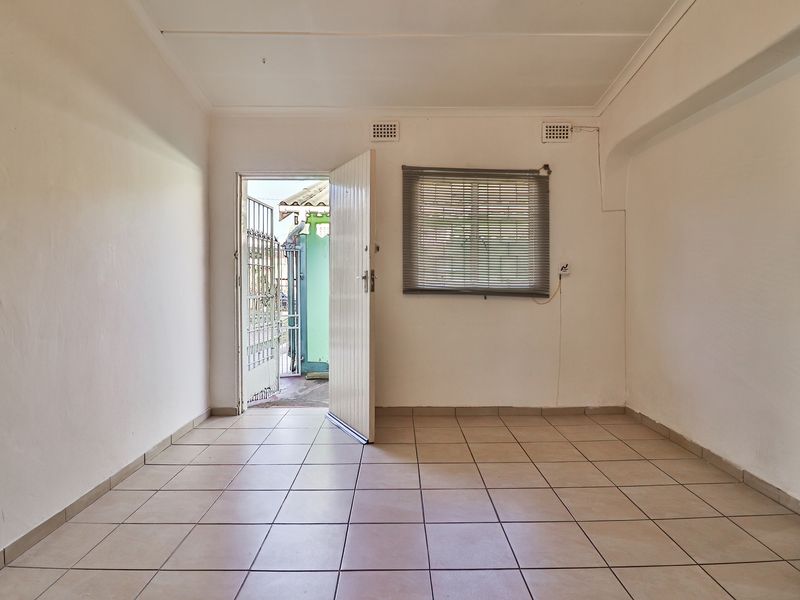 An empty, tiled living area featuring a security gate entrance and natural light, offering a blank canvas for interior design updates.