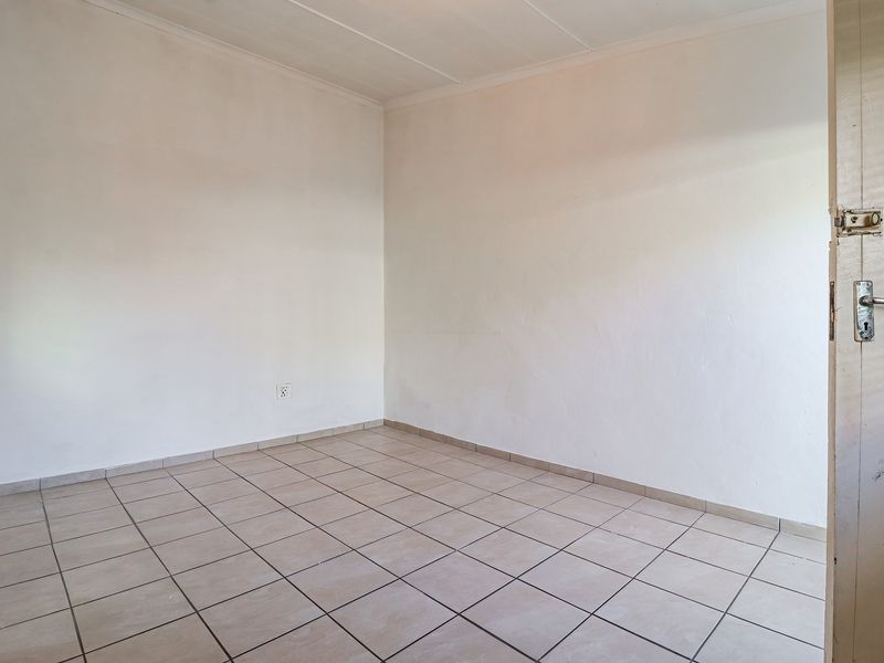 An empty bedroom featuring neutral ceramic floor tiles and plain white walls, ready for personalization.