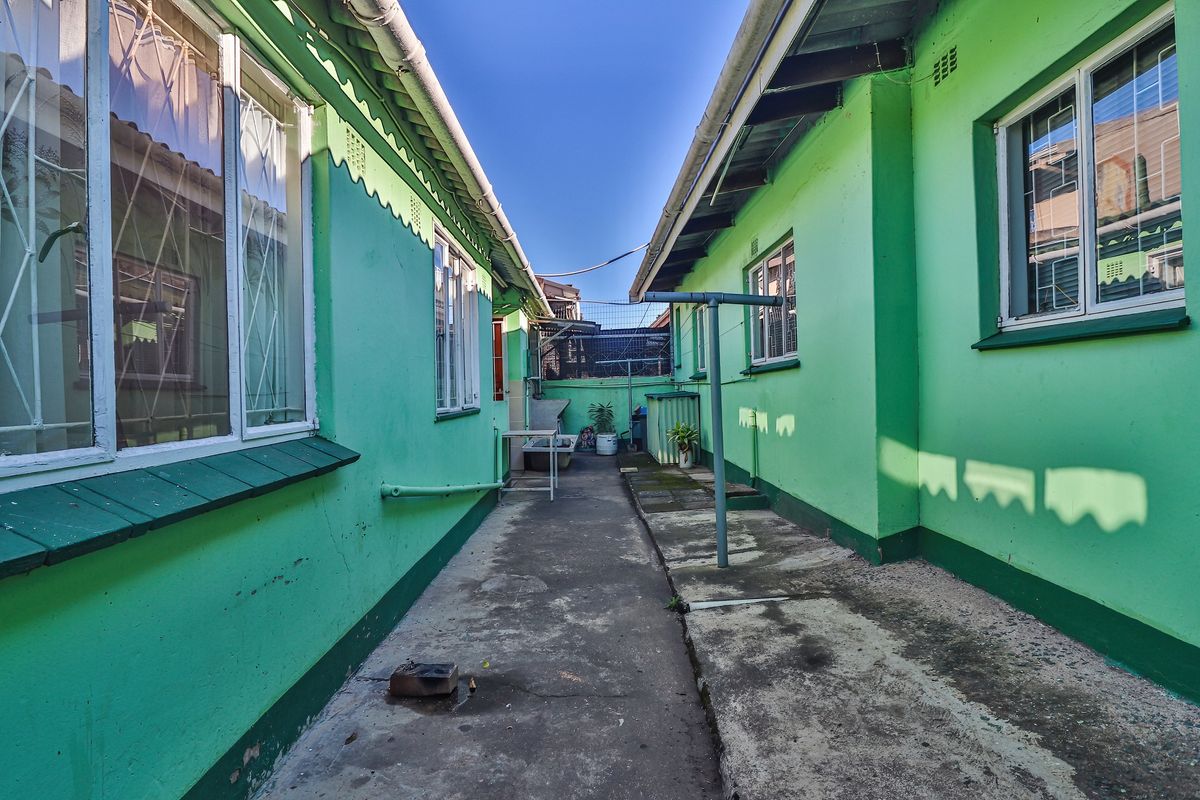 A narrow exterior rear walkway between two sections of the townhouse, featuring concrete paving, security-barred windows, and a fixed metal washing line.