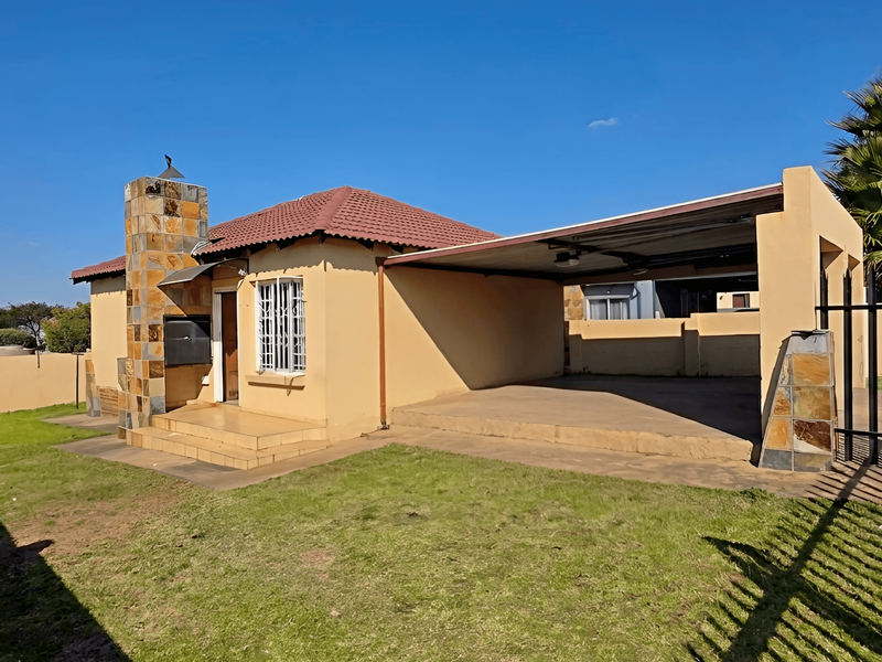 Front view of a single-story house featuring a tiled roof, stone-clad chimney, attached carport, and secure perimeter fencing with a gated entrance.