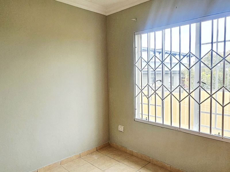 An empty bedroom featuring tiled flooring, a built-in cupboard, and a window fitted with security bars.