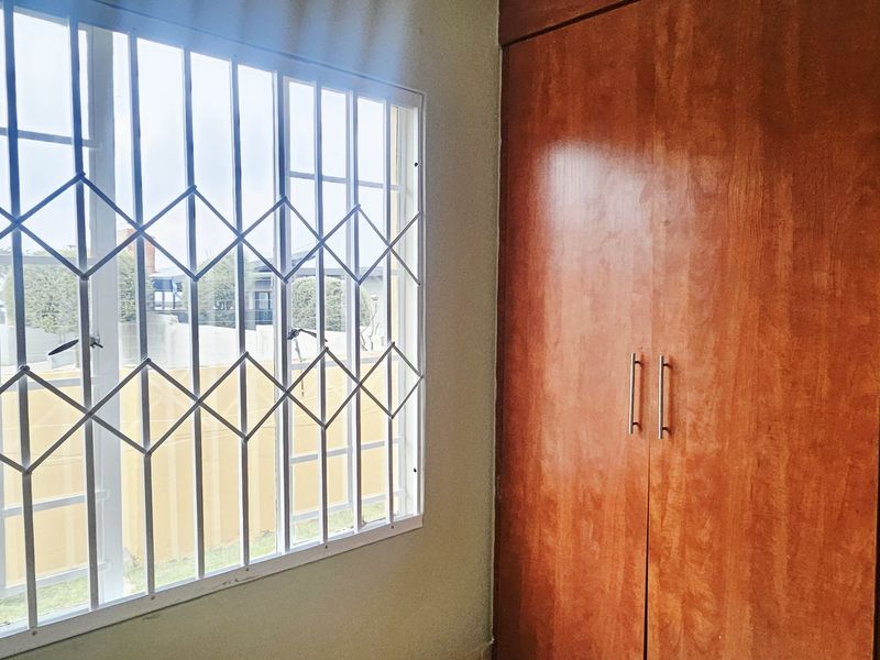 A clean, empty bedroom featuring a built-in wooden wardrobe and a window fitted with security bars.