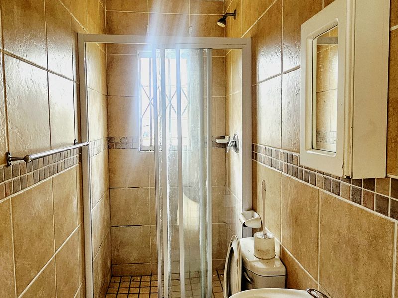 A compact bathroom featuring floor-to-ceiling tiled walls, a glass-enclosed shower, a wall-mounted medicine cabinet, and standard sanitary fixtures.