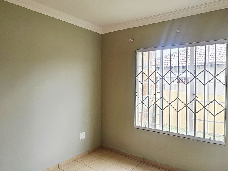 A vacant bedroom featuring tiled flooring, neutral wall paint, and a window fitted with a security gate.