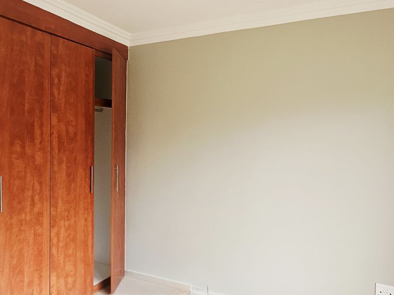 A clean, empty bedroom featuring neutral walls, coving, and a large built-in wooden wardrobe with modern handles.