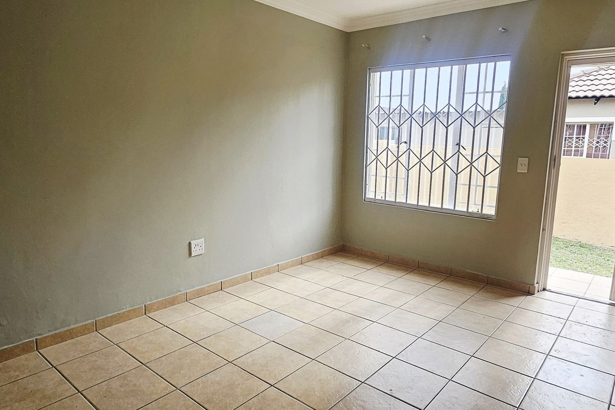 An empty bedroom featuring ceramic floor tiles, security gate access to the exterior, and fitted burglar bars on the window.