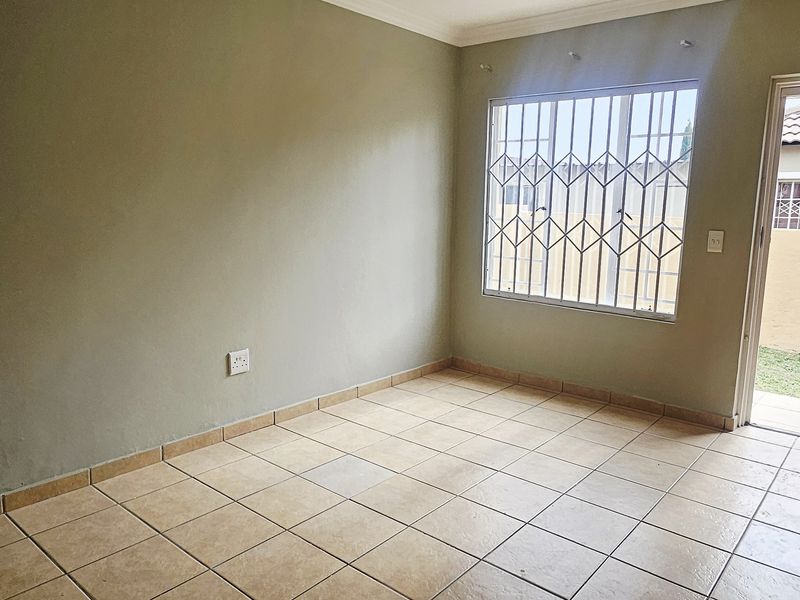 An empty bedroom featuring ceramic floor tiles, security gate access to the exterior, and fitted burglar bars on the window.