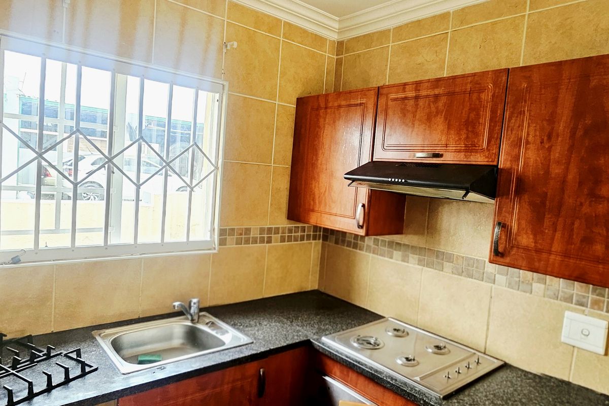 A functional kitchen featuring built-in wooden cabinetry, a gas hob with extractor fan, stainless steel sink, and tiled wall finishes.
