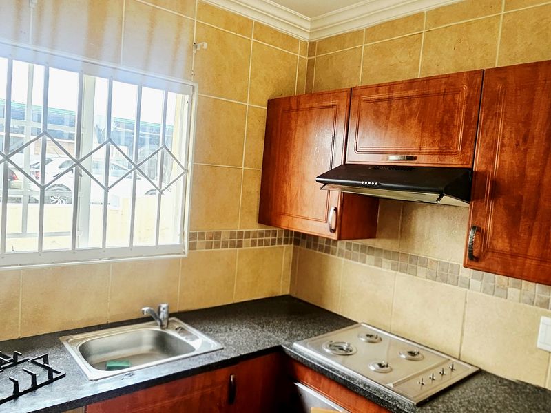 A functional kitchen featuring built-in wooden cabinetry, a gas hob with extractor fan, stainless steel sink, and tiled wall finishes.