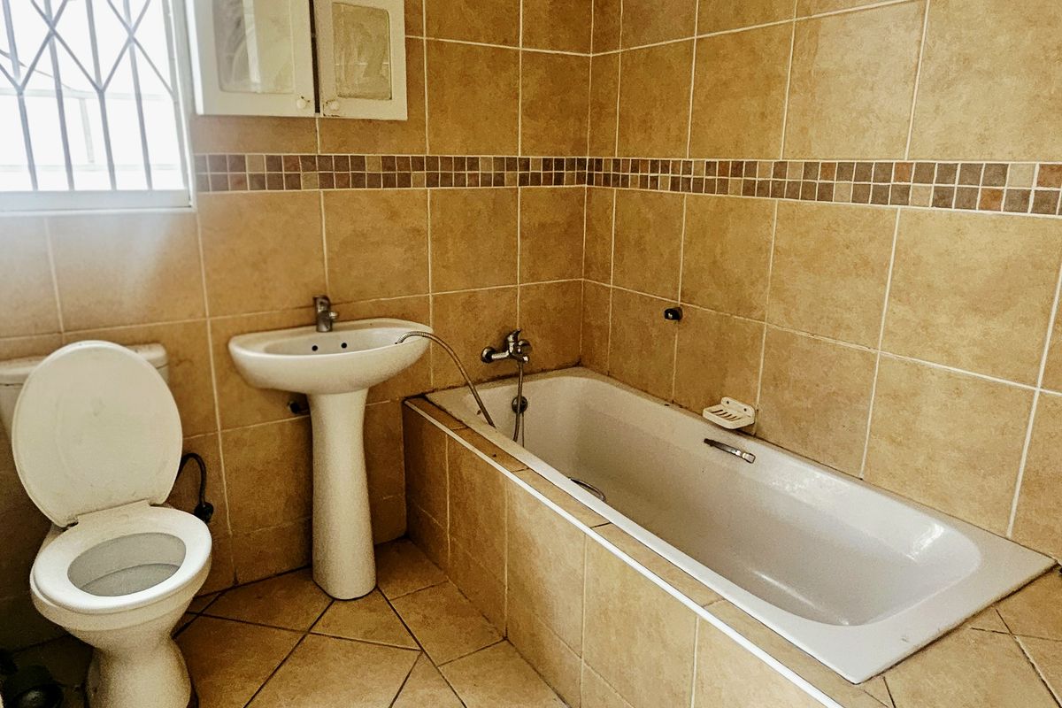 A functional bathroom featuring a built-in bathtub, pedestal basin, and tiled finishes, requiring minor repairs to fixtures and door frame.