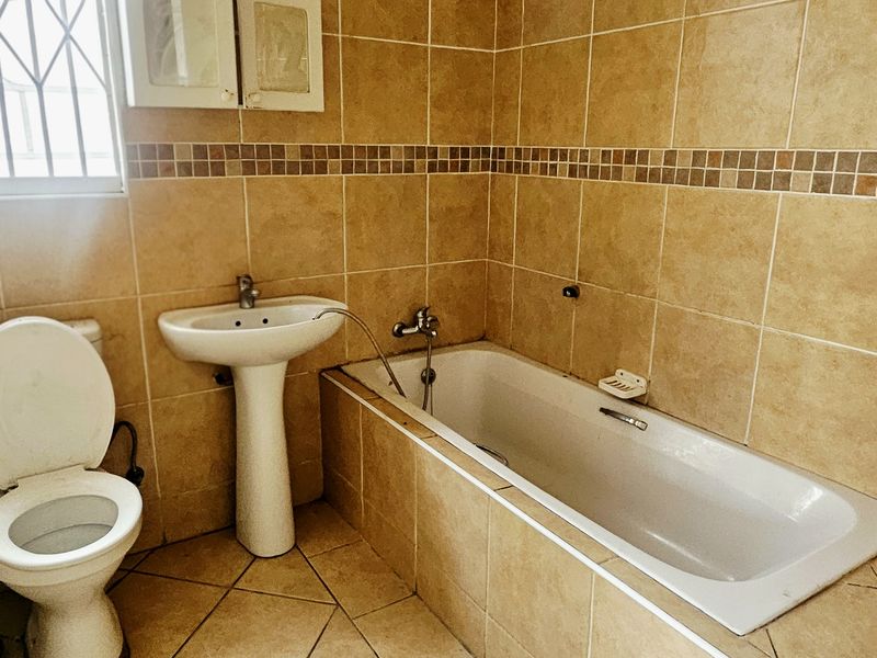 A functional bathroom featuring a built-in bathtub, pedestal basin, and tiled finishes, requiring minor repairs to fixtures and door frame.