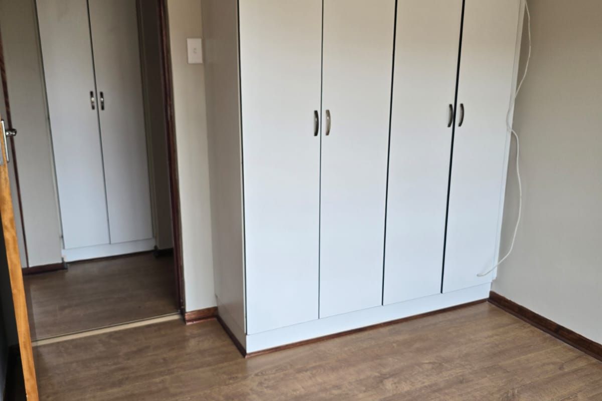 A bedroom featuring built-in white cabinetry and wood-look laminate flooring, with an adjacent doorway leading to a secondary closet area.