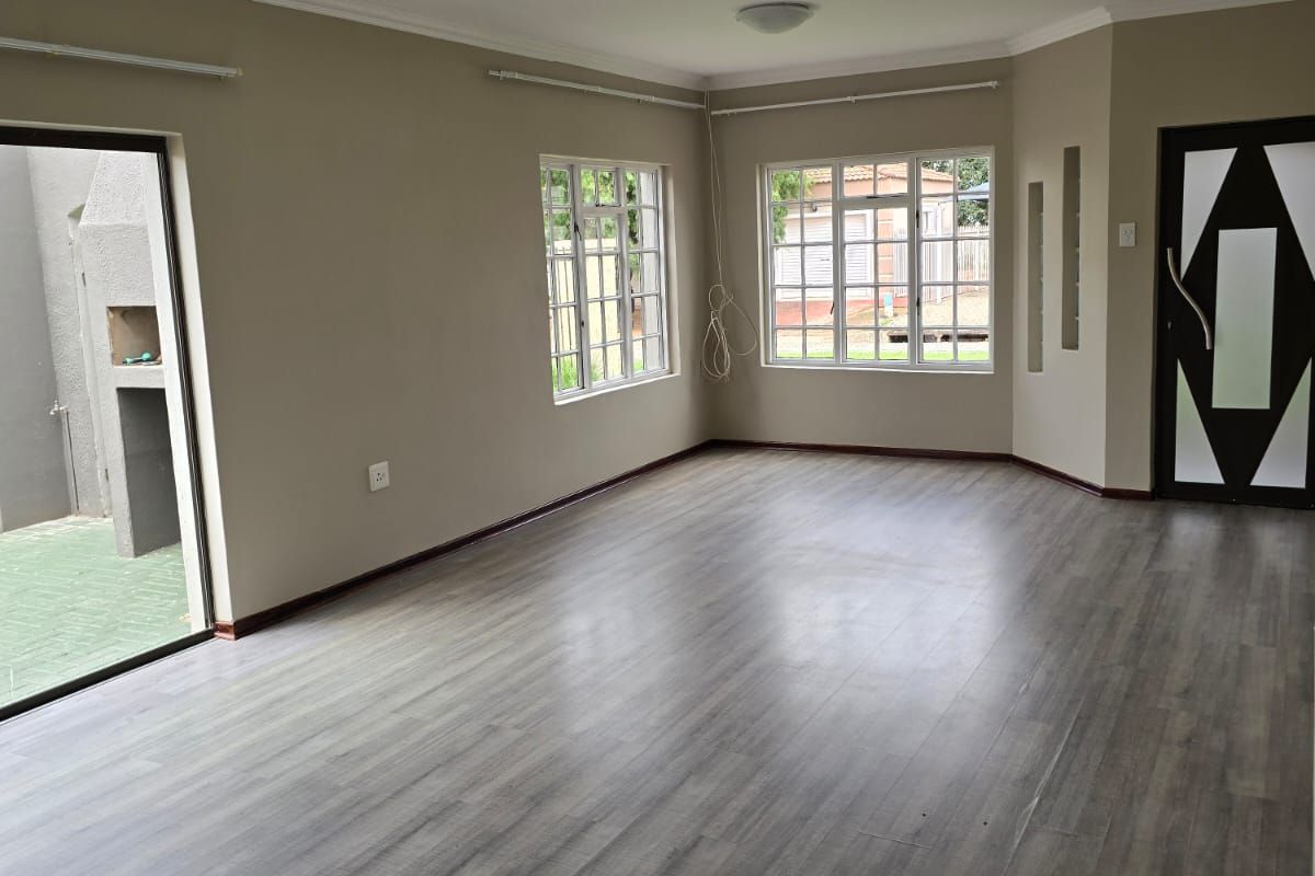Spacious living area featuring modern wood-look laminate flooring, large windows for natural light, and direct access to an outdoor patio area.