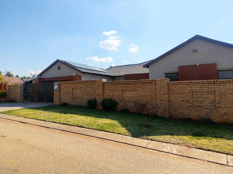 Front exterior view of a modern house featuring a face brick boundary wall, tiled roof, solar panels, and a secure metal driveway gate.